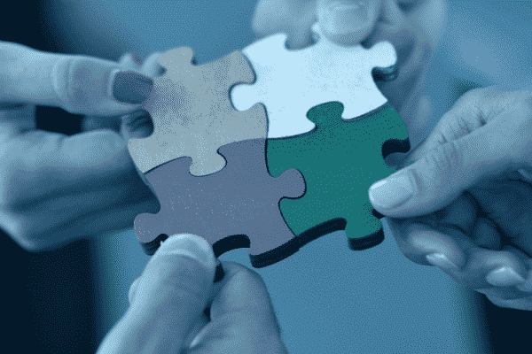 image of a puzzle with four pieces. Four hands, each hand is holding one piece of the puzzle.